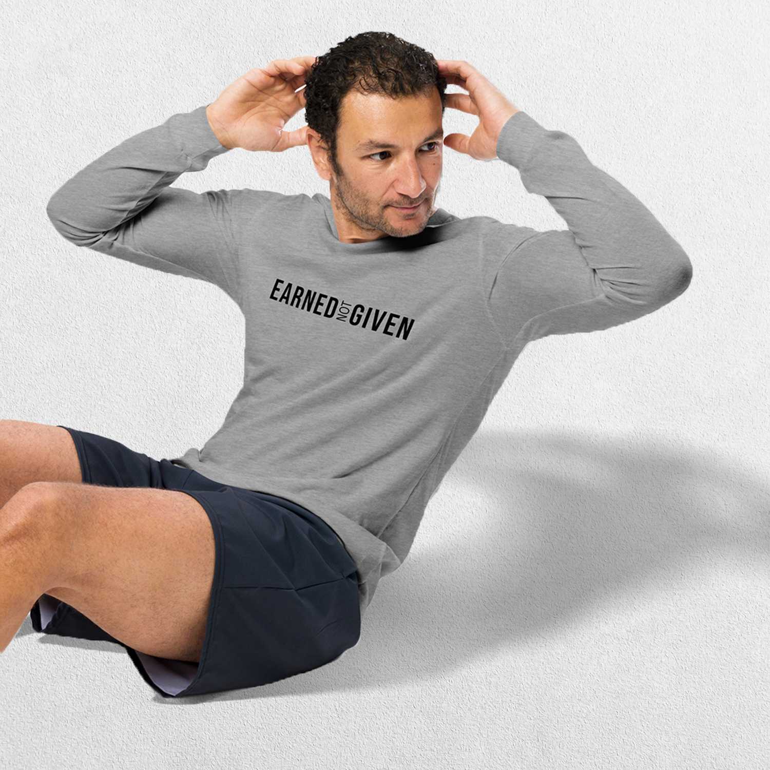 Exercising Model Wearing Athletic Heather GPW Earned Not Given Unisex Motivational Long Sleeve Tee in a studio background