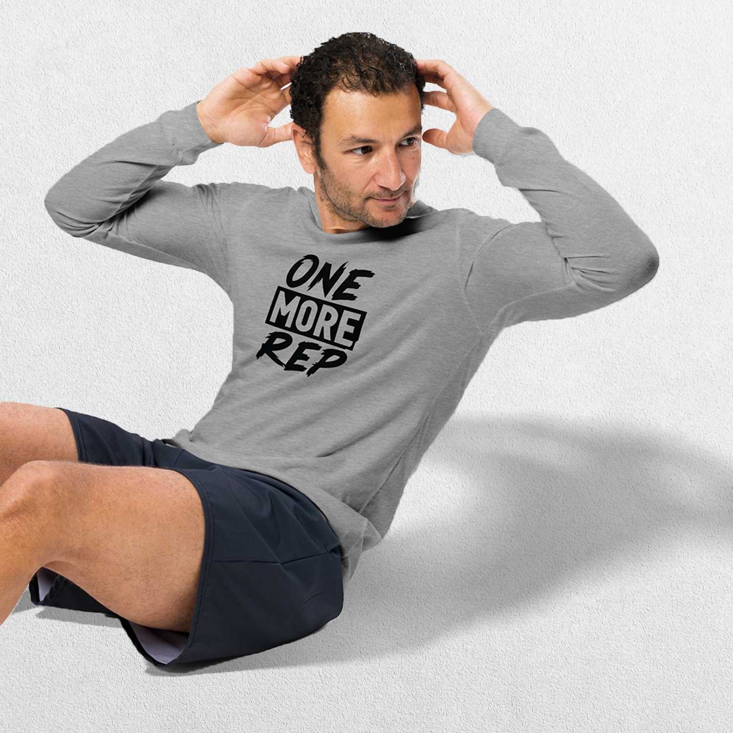 Exercising Model wearing the Athletic Heather GPW One More Rep Unisex Motivational Long Sleeve Tee with jeans in studio background.