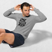 Exercising Model wearing the Athletic Heather GPW One More Rep Unisex Motivational Long Sleeve Tee with jeans in studio background.