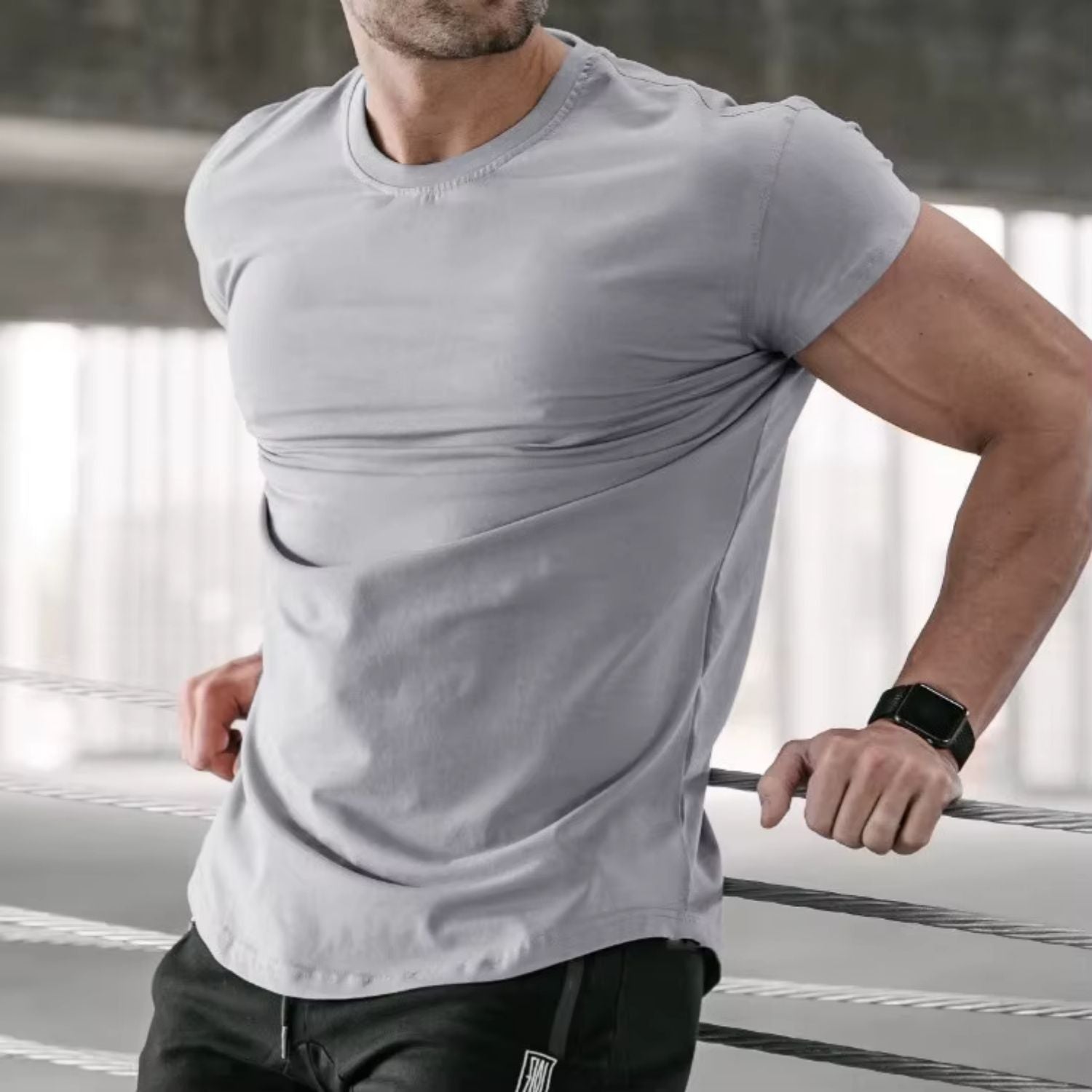 Close-up of a model in a dim grey gym t-shirt leaning on a railing, highlighting the soft cotton fabric and modern style.
