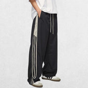 Black vintage Y2K baggy track trousers with elastic waistband modeled with hands in pockets for a casual look.