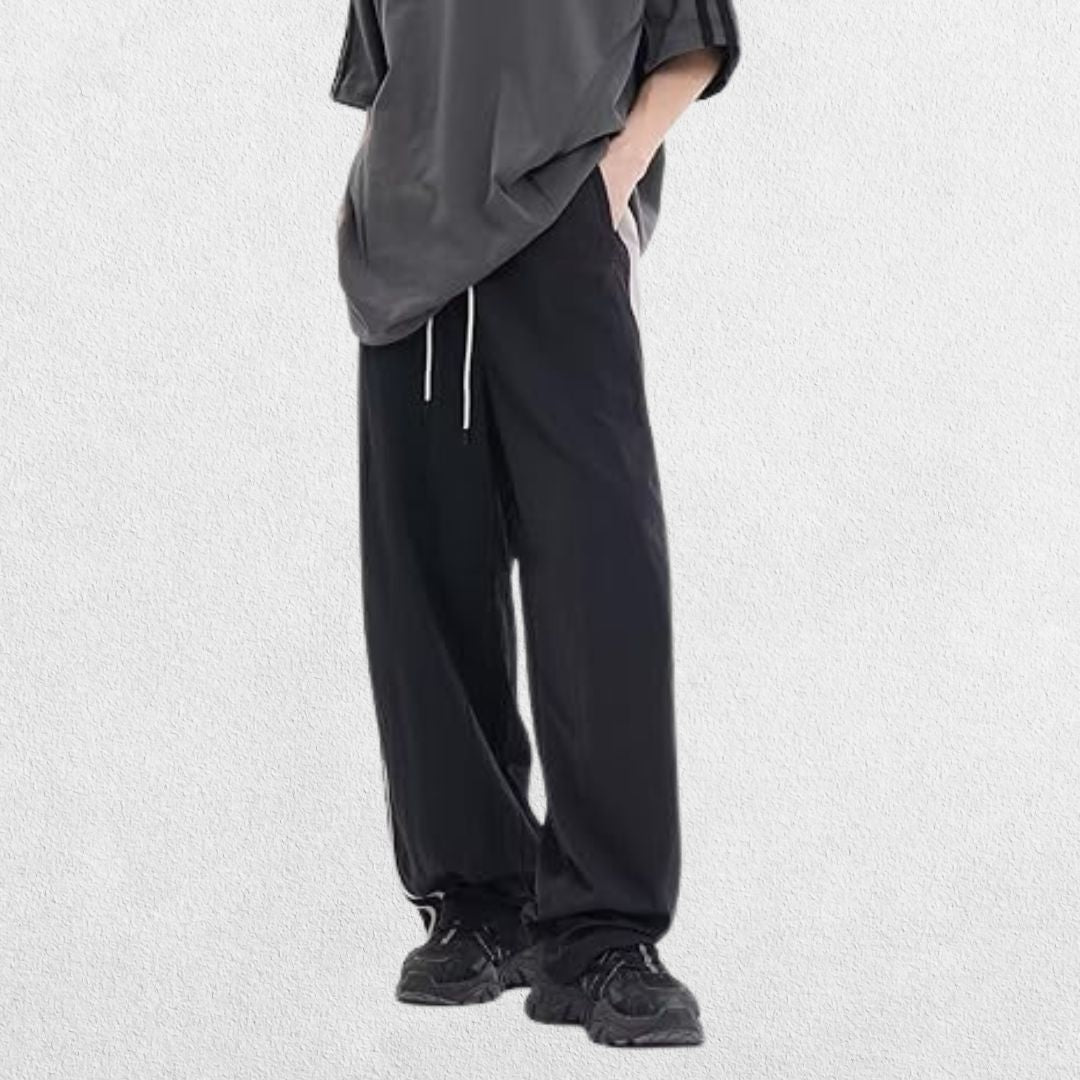 Model wearing Unisex Y2K Trousers in black with vintage baggy fit, hands in pockets, showcasing elastic waistband and retro streetwear style